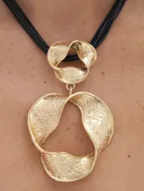 Collar dorado con colgante circular con diseño abstracto y textura labrada. El collar es de cordón negro.