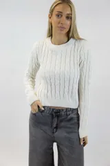 Buzo de chenille color blanco, con cuello redondo, mangas largas y diseño tejido con trenzas verticales en el frente y las mangas. Cuenta con terminaciones acanaladas en el cuello, los puños y la cintura.