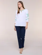 Blusa blanca de silueta semi entallada, confeccionada en tejido texturado. Cuenta con escote en V con abertura y vivo bordado multicolor, mangas 3/4 abullonadas con bordados, calados y puños elásticos.