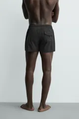 Short de baño negro de tejido técnico con estructura ripstop resistente a desgarros, cintura ajustable con cordón y bolsillos laterales.