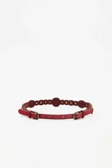 Cinturón de cuero rojo con apliques metálicos circulares y ovalados grabados a lo largo de toda la tira.