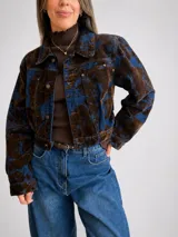 Campera corta de denim con diseño marmolado en tonos azul y marrón, de corte clásico con cierre frontal de botones metálicos y bolsillos en el pecho.