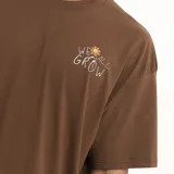 Remera marrón con estampado pequeño en el pecho que dice "We all grow" con una flor.