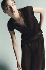 Top color marrón oscuro, con escote en V y mangas cortas. Presenta detalles de pliegues verticales en el delantero y terminaciones con encaje a tono en el escote y el ruedo inferior.