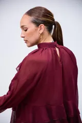 Blusa de gasa color bordó con cuello alto, mangas largas con volados y diseño de capas con volados en el cuerpo.