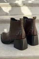 Bota corta de cuero color bordó, con taco cuadrado negro y suela de plataforma. Presenta detalles de tachas metálicas plateadas a lo largo de la costura frontal y lateral, con cierre interno.