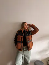 Campera negra de cuero sintético con cuello, solapas, puños y bolsillos de corderito color marrón.