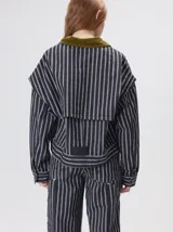 Campera de denim a rayas verticales con cuello de pana en color bordó. Presenta cierre frontal, mangas desmontables con cierre en los hombros, canesú en el pecho y bolsillos de parche cuadrados.