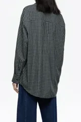 Camisa larga de corte recto, confeccionada en algodón, con patrón de cuadros pequeños en tonos azul marino y amarillo claro. Presenta cuello camisero, cierre frontal con botones y mangas largas con puño y botonadura.