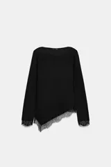 Top de manga larga y cuello redondo, confeccionado en tejido suave de color negro. Presenta un diseño de bajo asimétrico decorado con un delicado detalle de encaje a tono, que también se encuentra en los puños.