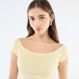 Camiseta de manga corta amarilla de punto calado, con escote bote y un pequeño lazo decorativo en el centro del pecho.