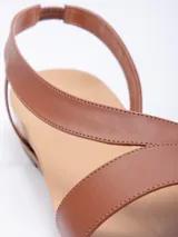 Sandalia baja de símil cuero color marrón, con doble cinta ancha cruzada sobre el empeine y tira elástica para ajuste en el tobillo.