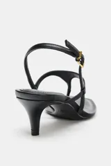 Sandalia de piel color negro con diseño de tiras finas, incluyendo una tira separadora para el dedo y una tira trasera ajustable con hebilla metálica. Presenta un tacón kitten fino y punta cuadrada.