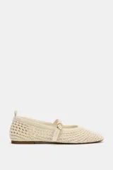 Zapatos planos tipo bailarina de color beige, confeccionados en tejido con efecto trenzado. Presentan una tira en el empeine con hebilla metálica dorada, tirador trasero y suela plana.