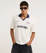 Remera de manga corta con cuello polo contrastante en azul marino y abertura en V. El cuerpo de la prenda es color crema y lleva un estampado frontal con la palabra "WONDER".
