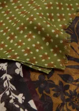 Pañuelo de tejido fluido de poliéster, con diseño estampado en bloques que combinan patrones florales, geométricos y franjas en tonos verde, marrón y negro, con terminaciones deshilachadas.