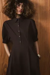 Vestido midi de algodón con cuello solapa, cierre frontal con botones y mangas cortas abullonadas con puños. Presenta un diseño evasé con bolsillos laterales ocultos y elástico en la espalda.