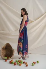 Vestido largo de gasa estampada con flores en tonos lila y rojo sobre fondo azul. Tiene cintura elastizada y cuello halter.
