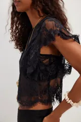 Top corto blanco confeccionado en encaje de nailon con diseño floral transparente, escote redondo y mangas cortas holgadas con terminación festoneada.