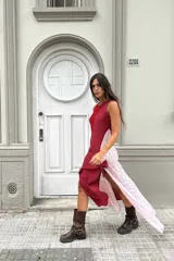 Vestido largo de encaje blanco con forro interior blanco, abertura lateral y detalle de lazo negro en la pierna. Se complementa con botas de cuero negras, chaqueta de cuero negra con flecos y gafas de sol negras.