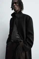 Abrigo negro de corte recto confeccionado en tejido con lana. Tiene cuello alto, manga larga con puños abotonados, bolsillos laterales y abertura en la espalda. Cierre frontal con botones.