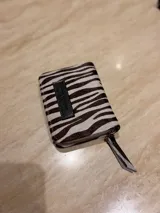Billetera de cuero de pelo con estampado animal print tipo cebra, cierre perimetral con tirador de cuero y etiqueta frontal de cuero negro.