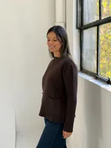 Sweater de punto color chocolate, con cuello redondo, manga larga y dos bolsillos frontales tipo parche.