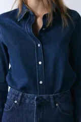 Camisa de denim de corte clásico con cuello solapa, manga larga con puños anchos y cierre frontal con botones. Presenta un diseño de bajo asimétrico.