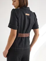 Chaqueta de lino color negro con silueta relajada, botones frontales, mangas cortas con puños y detalle de cinturón marrón con textura.