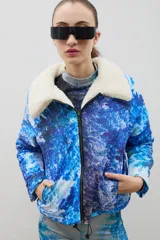 Campera con estampado de bosque en tonos azules, cuello de sherpa en color crema y cierre frontal con cremallera. Cuenta con elástico ajustable en la cintura.