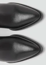 Botín de cuero vacuno color negro, con diseño de estilo western, punta fina y tacón bloque de 6,5 cm. Cuenta con cierre de cremallera lateral.