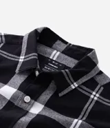 Camisa de franela de manga larga con estampado de cuadros en blanco y negro. Presenta cuello inglés, cierre frontal con botones y bolsillo en el pecho.