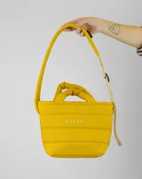 Bolsito tipo tote acolchado de color amarillo, con diseño de líneas horizontales y logo de la marca estampado en el frente. Cuenta con dos asas superiores acolchadas y una correa ajustable de cinta en color beige.