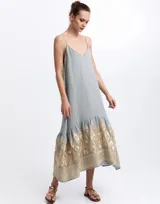 Vestido largo gris con tirantes finos, escote en V y silueta fluida, confeccionado en ramio, con detalle de bordado dorado en el bajo.