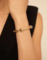 Pulsera rígida de diseño minimalista con cierre tipo grillete, fabricada en aleación de metales con baño de oro de 18k.