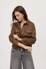 Campera negra de efecto gamuzado con cuello camisero, cierre frontal de botones, bolsillos plaqué en el pecho y detalles de costuras decorativas y calados.