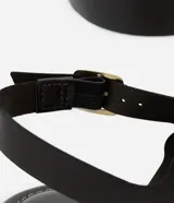 Sandalia plana tipo gladiadora color negro, confeccionada en poliuretano. Presenta tiras onduladas con recortes ahuecados y detalles de ojalillos y tachas metálicas doradas. Cuenta con doble tira ajustable en el tobillo con hebillas metálicas.