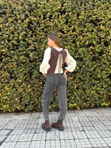 Chaleco de cuero marrón chocolate, sin mangas, con escote redondo y detalles de costuras decorativas en forma de espiga en el frente. Cuenta con cordones laterales para ajustar.