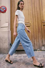 Jeans de tiro alto con corte barrel, pernera holgada que se estrecha hacia el tobillo y bajo deshilachado. Presenta costuras verticales decorativas en el frente y cierre frontal con cremallera y botón.