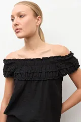 Blusa negra estilo bardot con escote de hombros descubiertos, detalles de volados fruncidos en el pecho y diseño sin mangas.