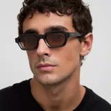 Lentes de sol con montura cuadrada de color negro y cristales polarizados en tono marrón. Presentan un diseño retro con parte superior plana y patillas con detalle sobresaliente.