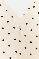 Vestido corto con estampado de lunares negros sobre fondo blanco crema. Presenta escote en V, tirantes finos y un volante fruncido en la parte inferior.