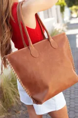 Bolso tote de cuero color tostado con costuras blancas a la vista en los laterales y doble asa de hombro.