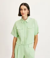 Camisa color verde claro de crepé, con cuello camisero, abotonado delantero, mangas cortas y solapas delanteras aplicadas.