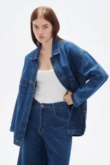 Sobrecamisa de jean en tono azul oscuro, con cuello clásico, cierre frontal de botones metálicos y mangas largas. Presenta un corte holgado y diseño versátil.