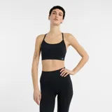 Top deportivo New Balance de soporte ligero, diseñado para yoga y actividades de bajo impacto. Presenta un diseño de espalda con tiras finas cruzadas, banda elástica inferior y logo de la marca en el frente.