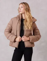 Campera puffer de corte recto y acabado mate, con diseño de bloques horizontales acolchados. Presenta capucha integrada con cordones de ajuste, cierre frontal metálico y bolsillos laterales invisibles. Incluye puños elásticos internos para mayor protección contra el frío.