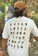 Remera blanca de algodón con cuello redondo y estampado en la espalda con imágenes de cogollos de marihuana y texto "BROKERS HIGH QUALITY GOODS".