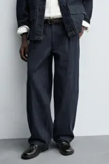 Pantalón de corte barrel fit confeccionado en denim de algodón rígido color azul oscuro. Presenta cintura con pliegues frontales, bolsillos laterales y bolsillos traseros de vivo. Cierre frontal con cremallera y gancho metálico oculto.