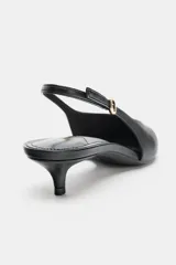 Zapato destalonado negro de punta fina con tacón kitten. Presenta un escote en pico y una tira trasera ajustable con hebilla y elástico.